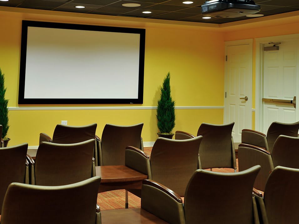 An empty conference room with arranged chairs facing a large projection screen.