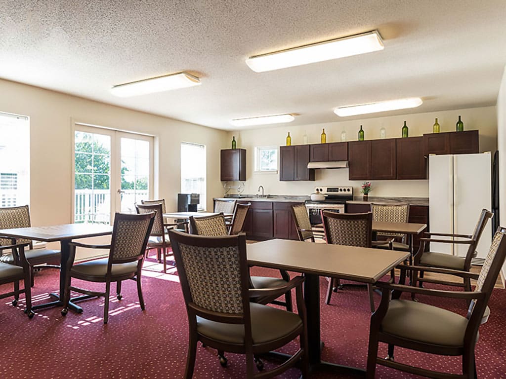 A spacious communal kitchen and dining area with several tables and chairs, featuring large windows and modern appliances.