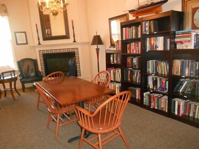 Cozy library room with a wooden table, chairs, bookshelves, and a fireplace.