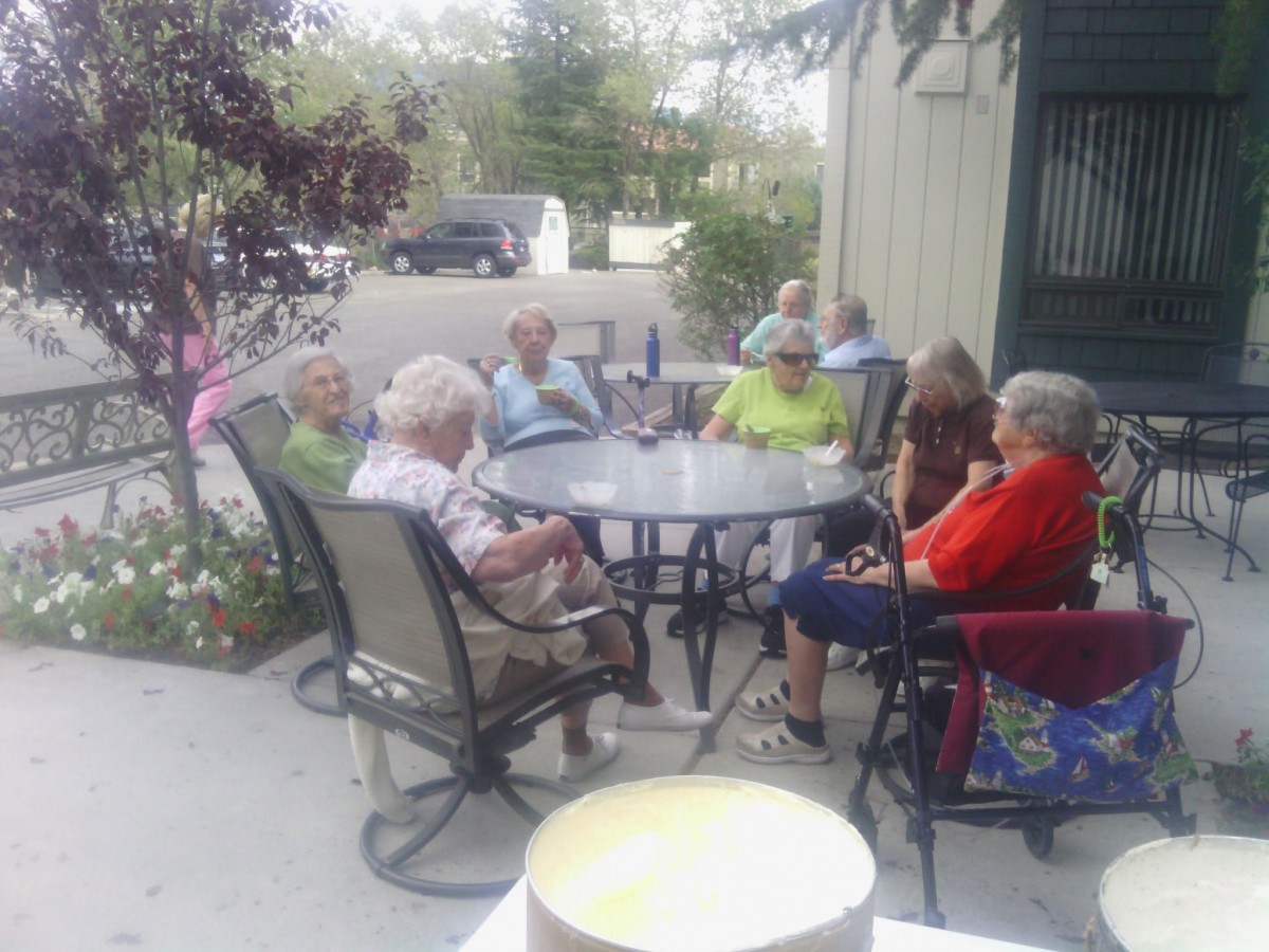 A group of seniors sitting around a table outdoors, engaged in conversation.