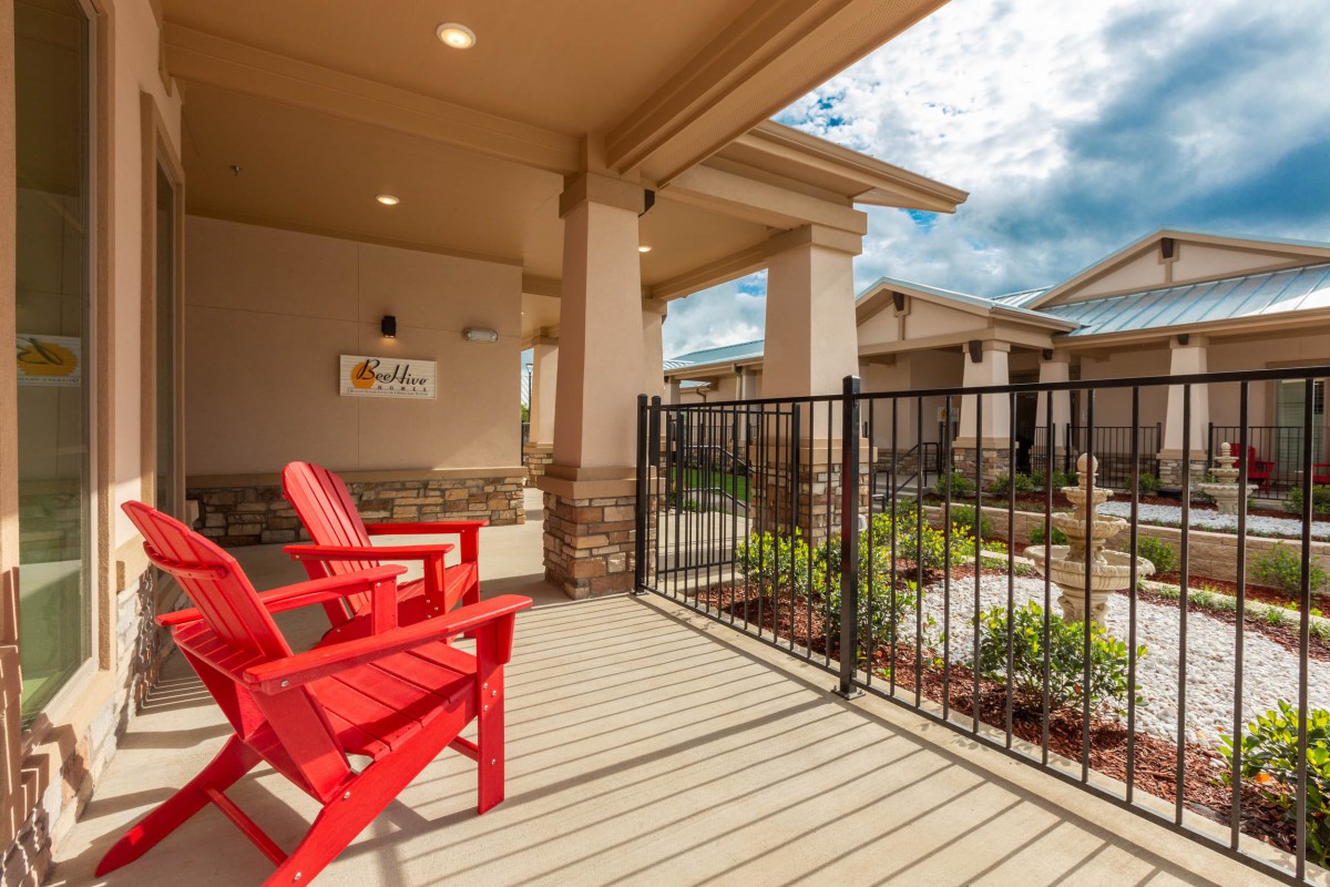 A cozy patio area with red chairs and a fenced garden view.