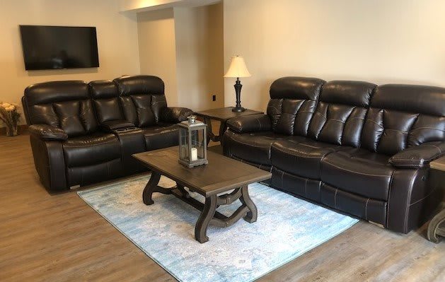 A cozy living room with black leather sofas, a wooden coffee table, and a lamp on side tables.