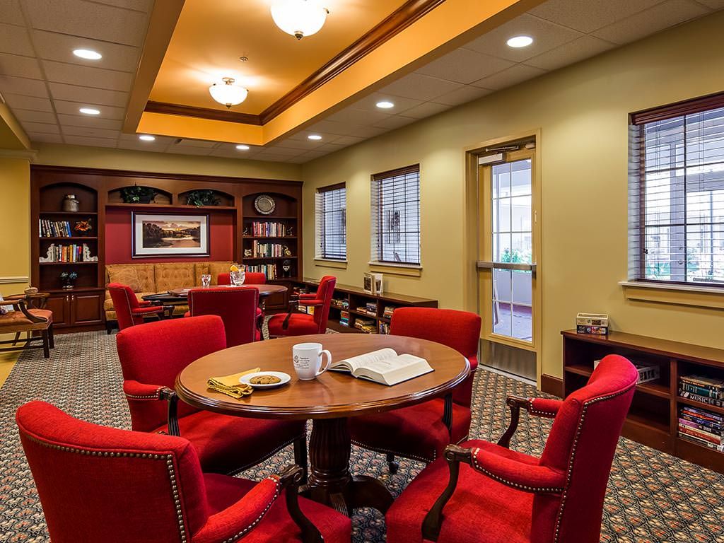 A cozy library room with red chairs, a round table, and bookshelves.