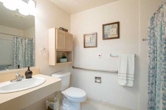 A clean and minimalist bathroom with a toilet, sink, mirror, towel rack, and wall art.