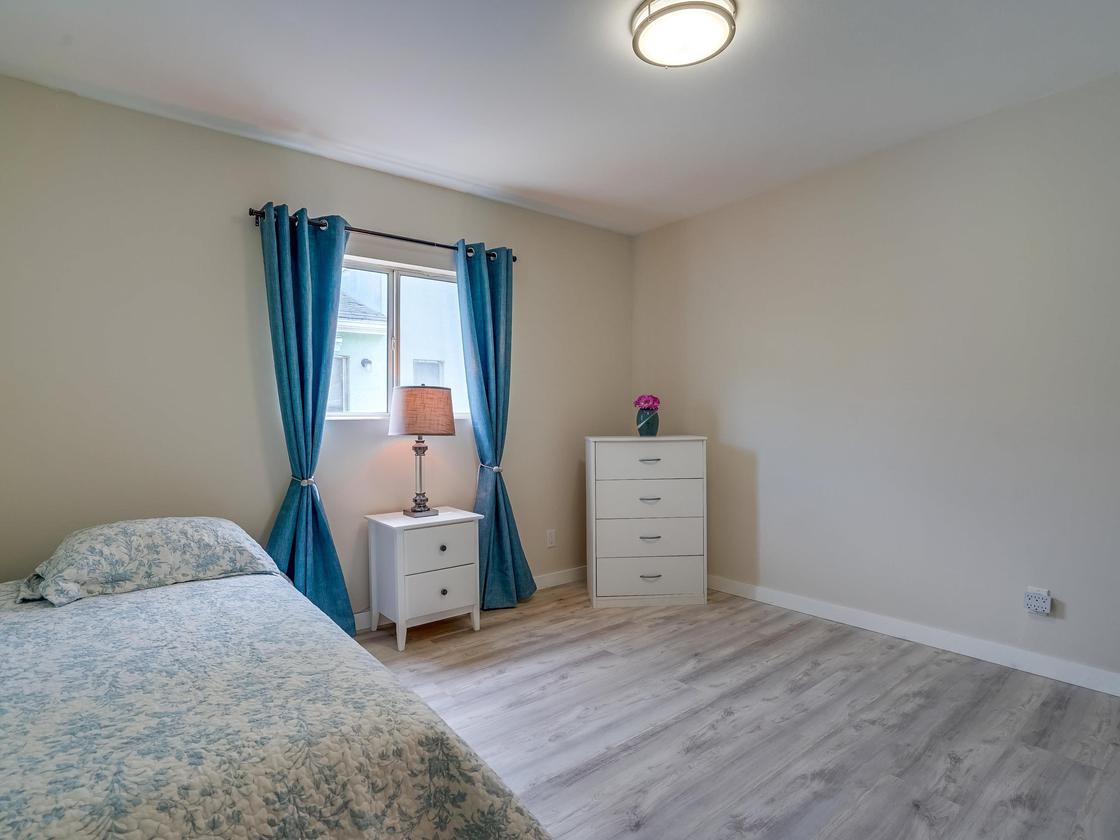 A minimalist bedroom with a bed, dresser, and nightstand by the window with blue curtains.