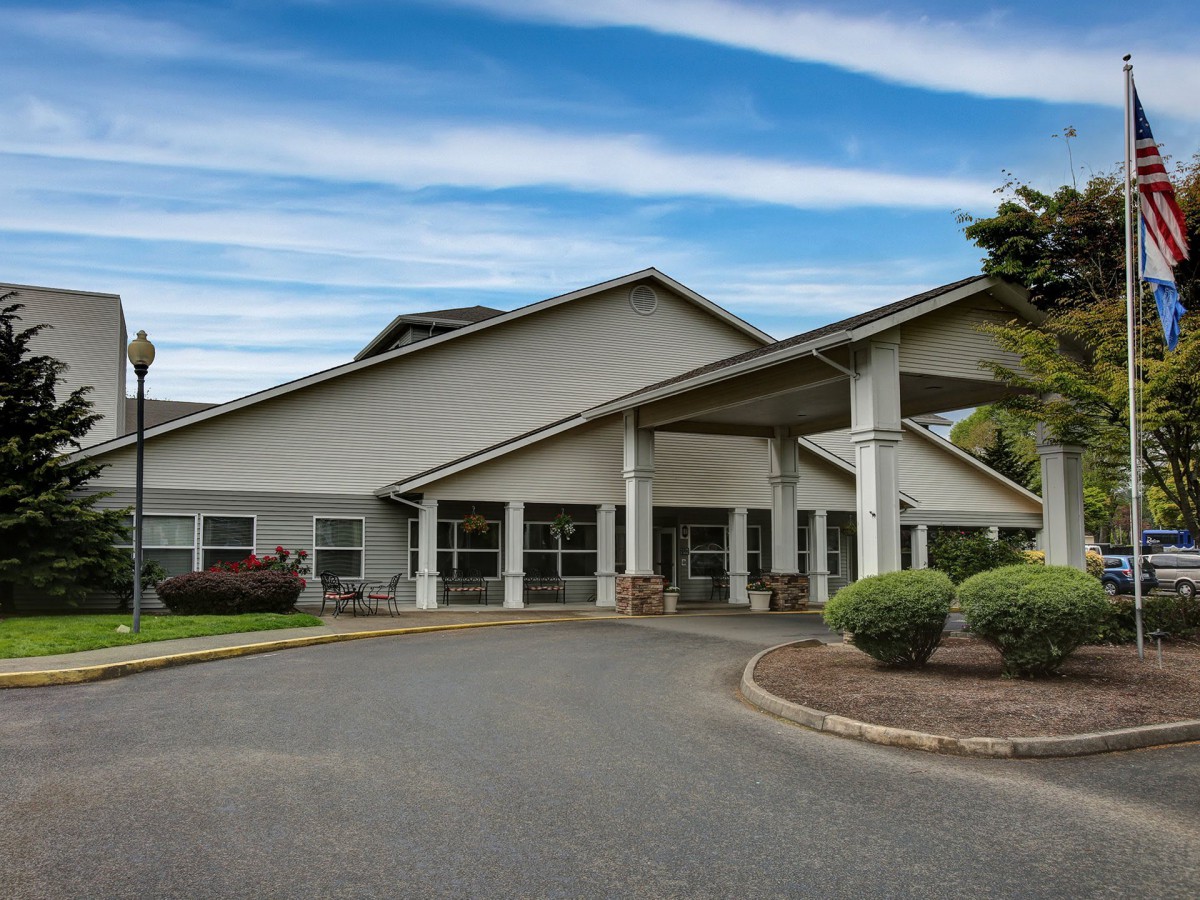 A modern building entrance with a circular driveway and landscaped surroundings under a partly cloudy sky.
