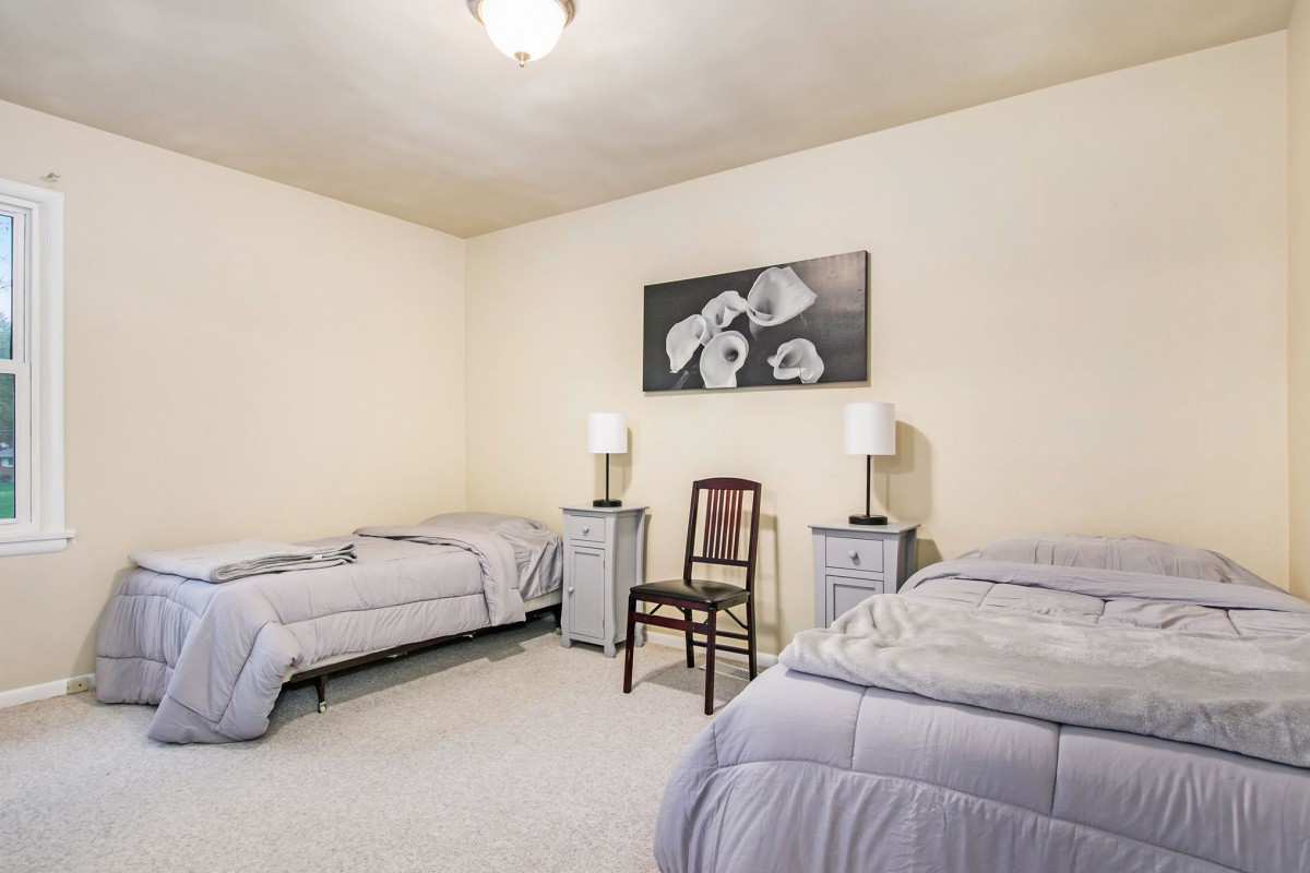 A simple bedroom with two twin beds, nightstands with lamps, and floral artwork on the wall.