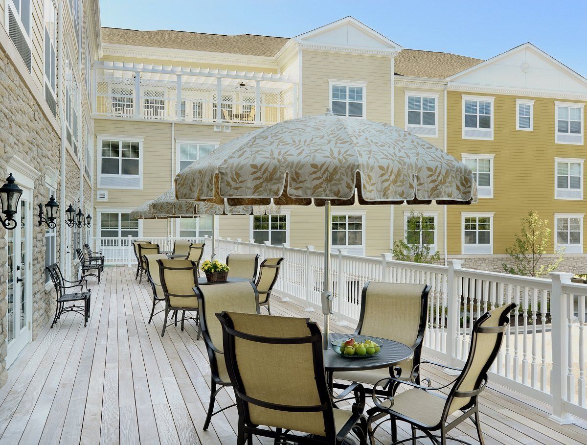 An outdoor patio area with tables, chairs, and umbrellas in front of a residential building.