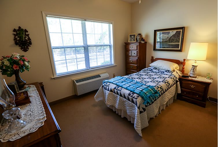 A cozy bedroom with a single bed, featuring a colorful quilt and a dresser by the window.