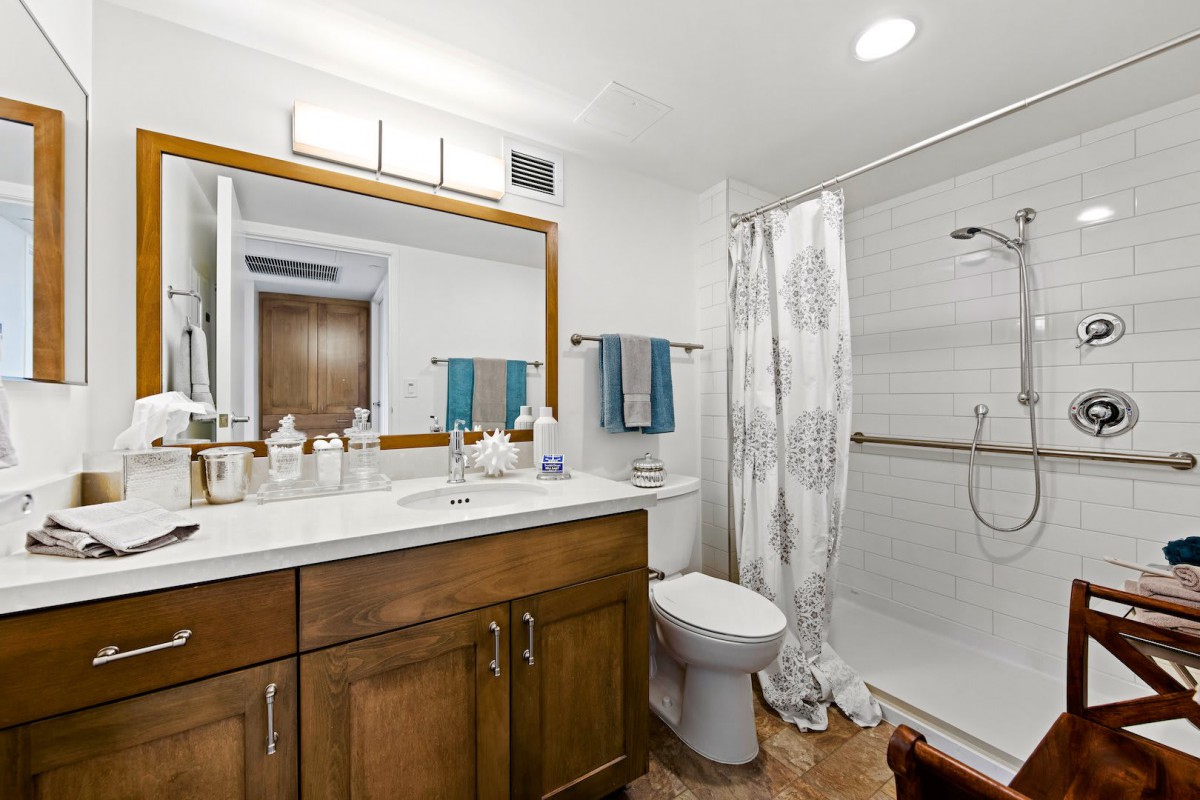 A modern bathroom with a wooden vanity, large mirror, and walk-in shower.