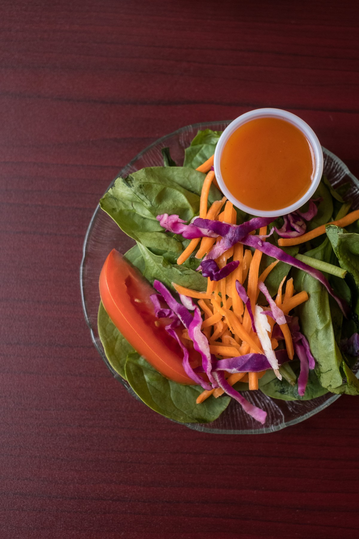 A fresh salad with spinach, carrots, red cabbage, tomato, and a side of dressing.