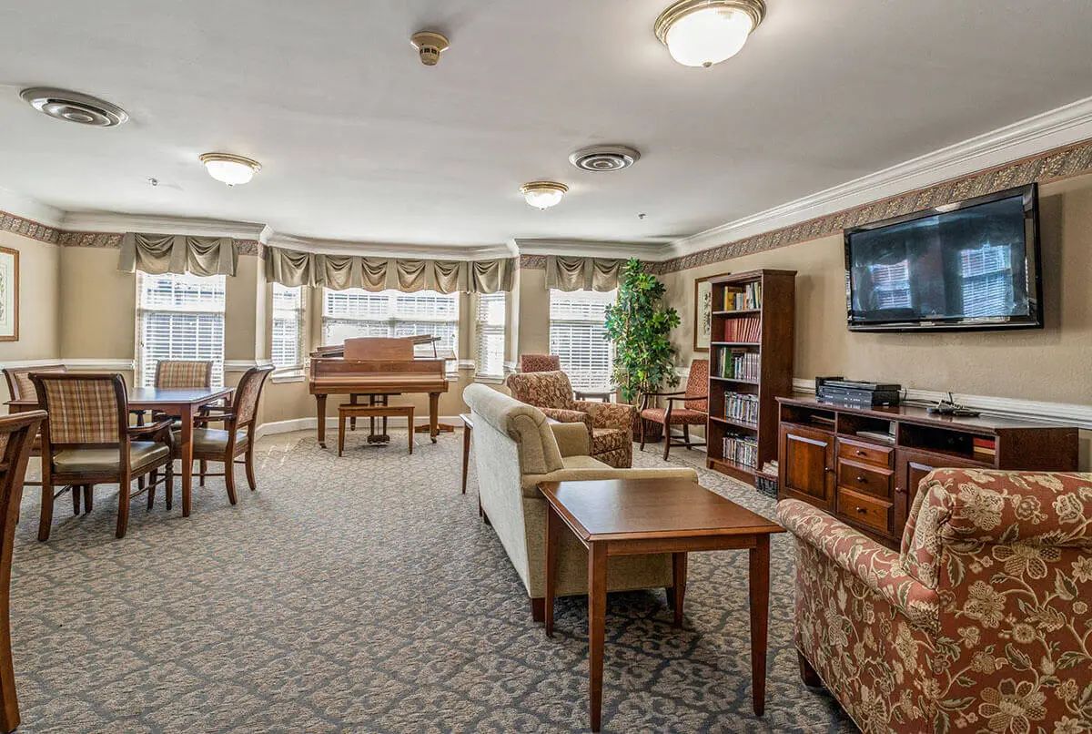 A spacious living room with comfortable seating, a piano, bookshelf, and television.
