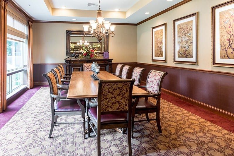 Elegant dining room with a long wooden table and upholstered chairs, featuring a chandelier and decorative artwork.