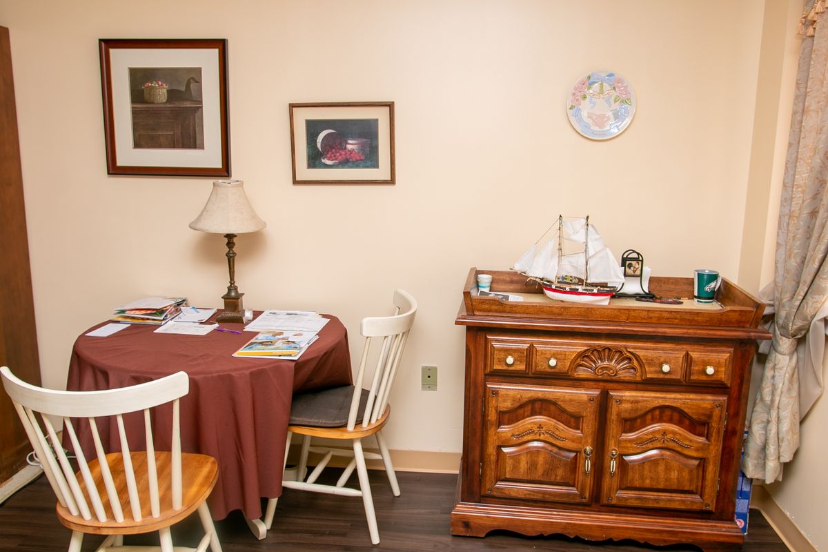 A cozy dining room with a round table, chairs, and wooden sideboard adorned with a model ship.