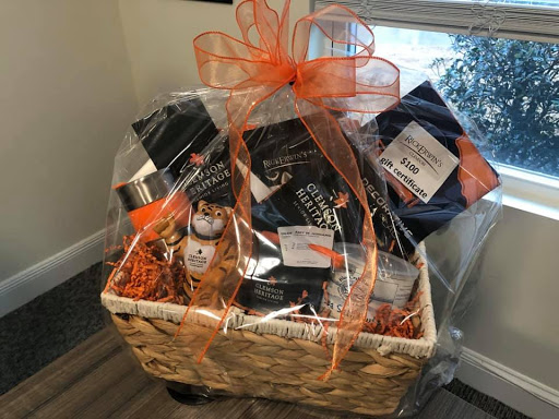 A beautifully arranged gift basket filled with an assortment of snacks and treats, wrapped in cellophane and adorned with a vibrant orange ribbon.