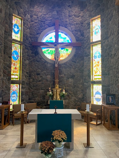 A serene interior of a church featuring a prominent cross, an altar, and beautifully designed stained glass windows.
