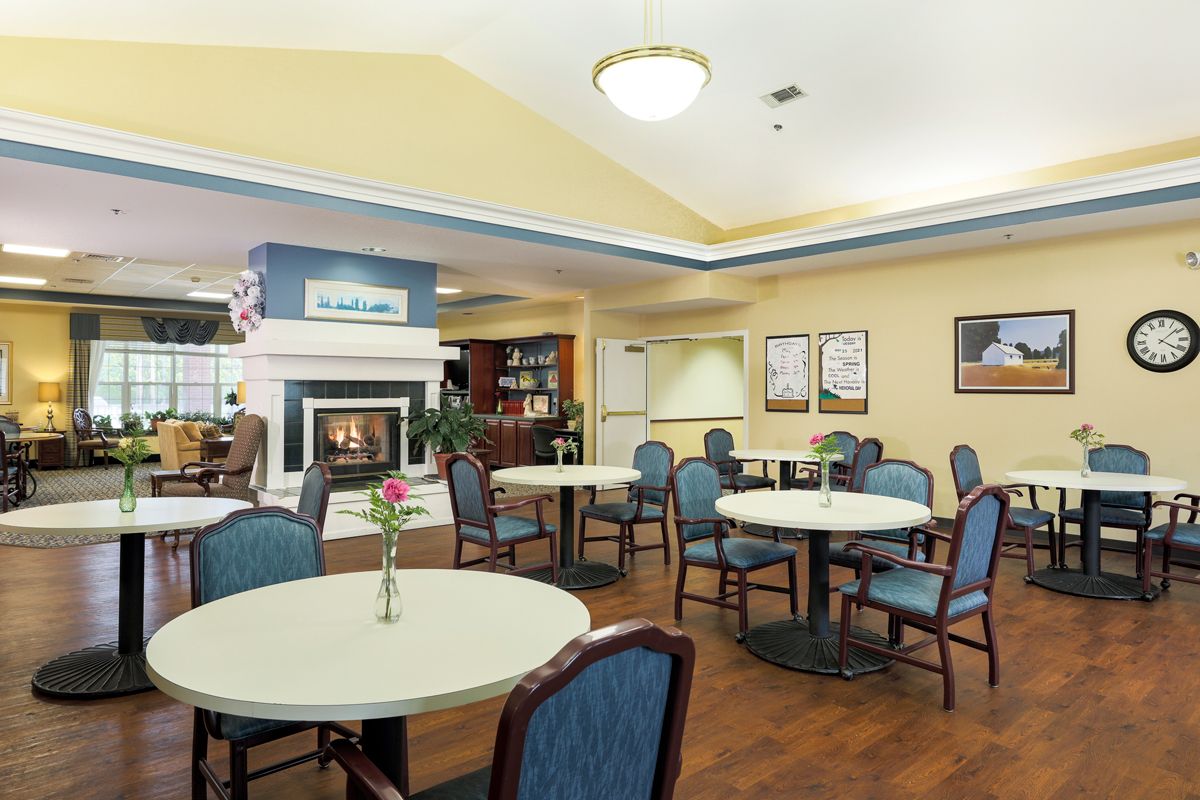 A cozy dining area with round tables and chairs, featuring a fireplace and warm decor.