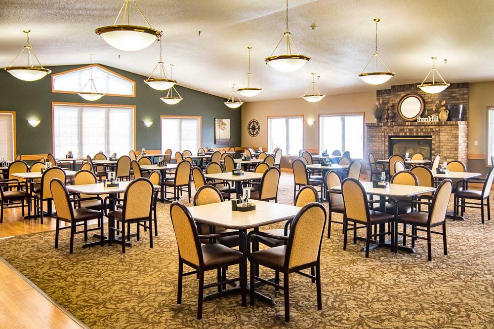 A spacious dining area with neatly arranged tables and chairs, illuminated by elegant chandeliers.