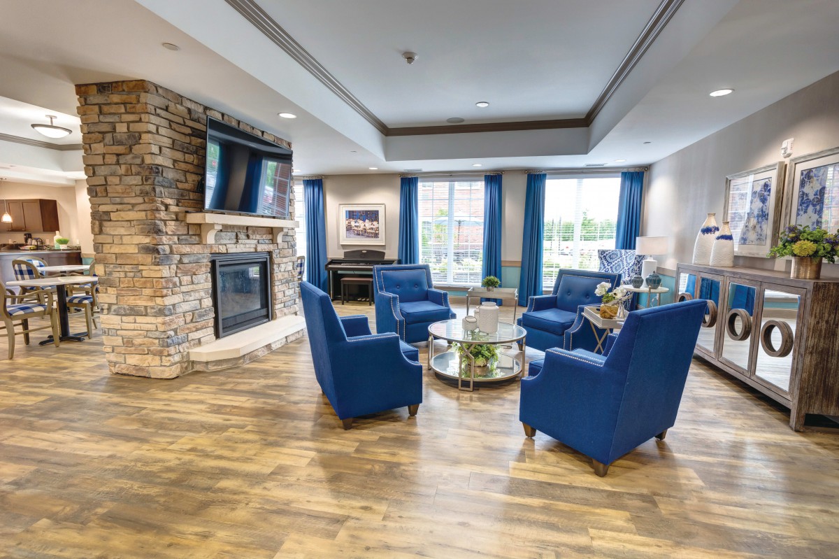 A cozy living room with blue chairs arranged around a coffee table, featuring a stone fireplace and wood flooring.