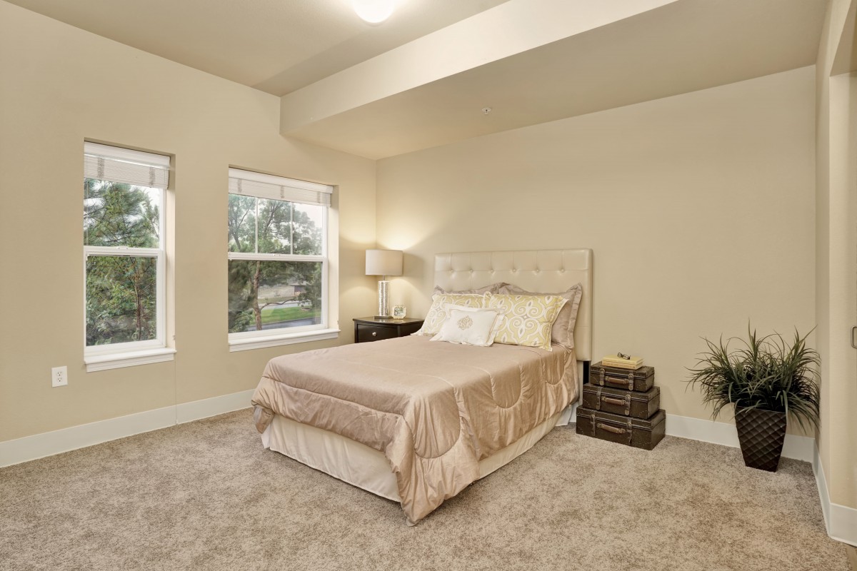 A cozy bedroom featuring a neatly made bed, soft carpets, and large windows allowing natural light to fill the room.