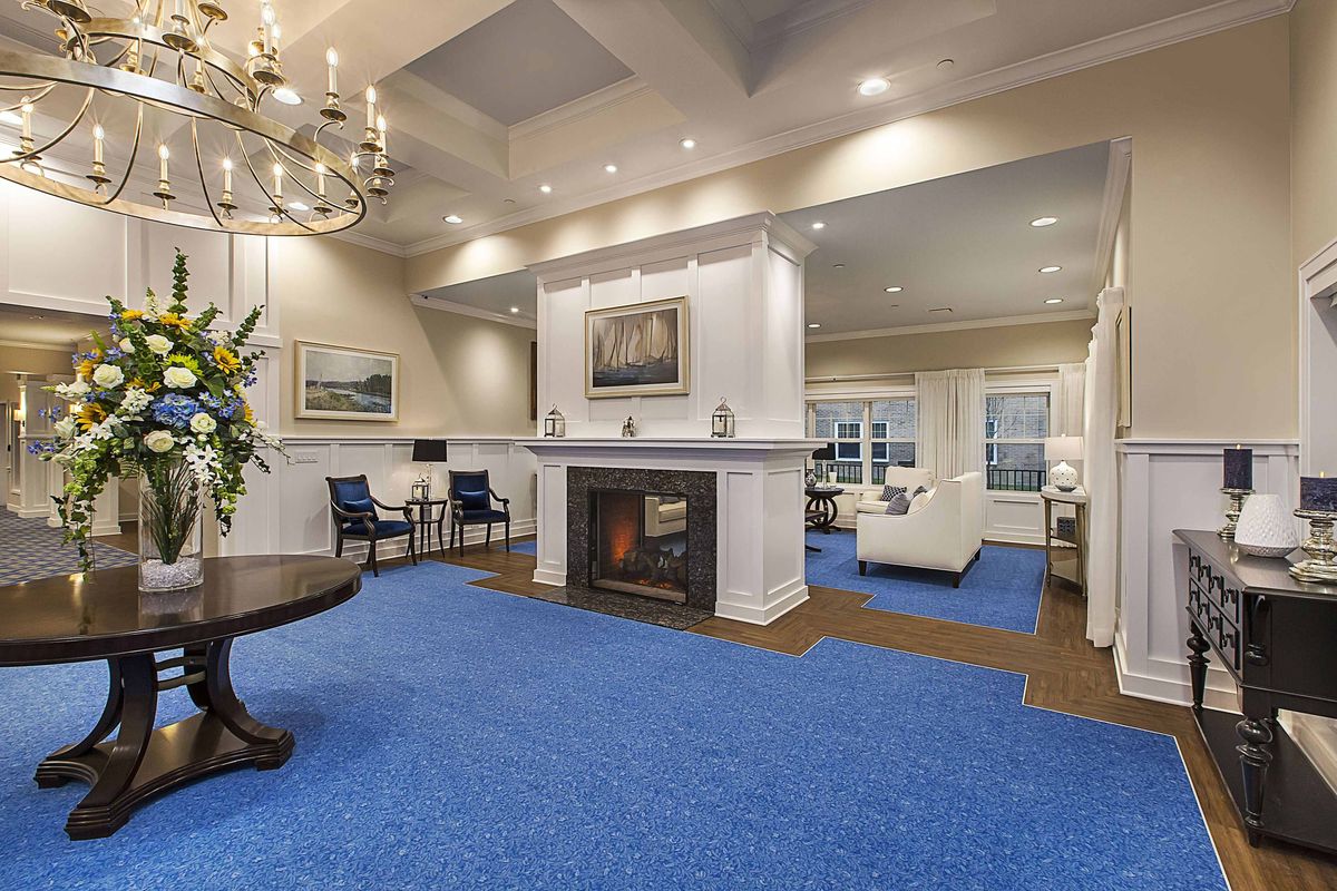 A spacious living room with a fireplace and blue carpet, featuring elegant lighting and seating areas.