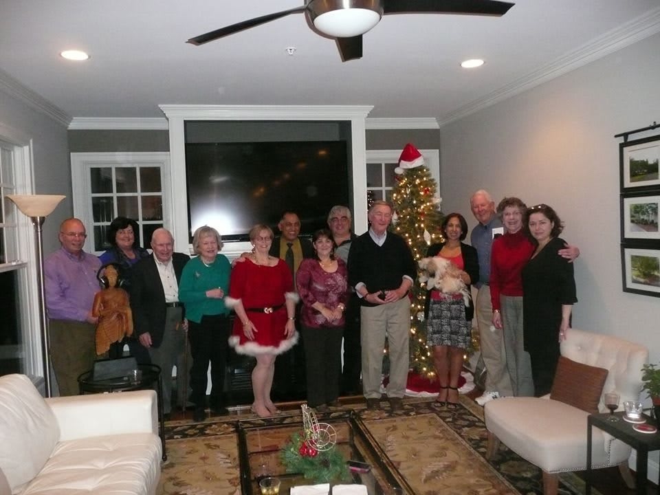 A group of people gathered in a living room celebrating Christmas, with a decorated tree in the background.