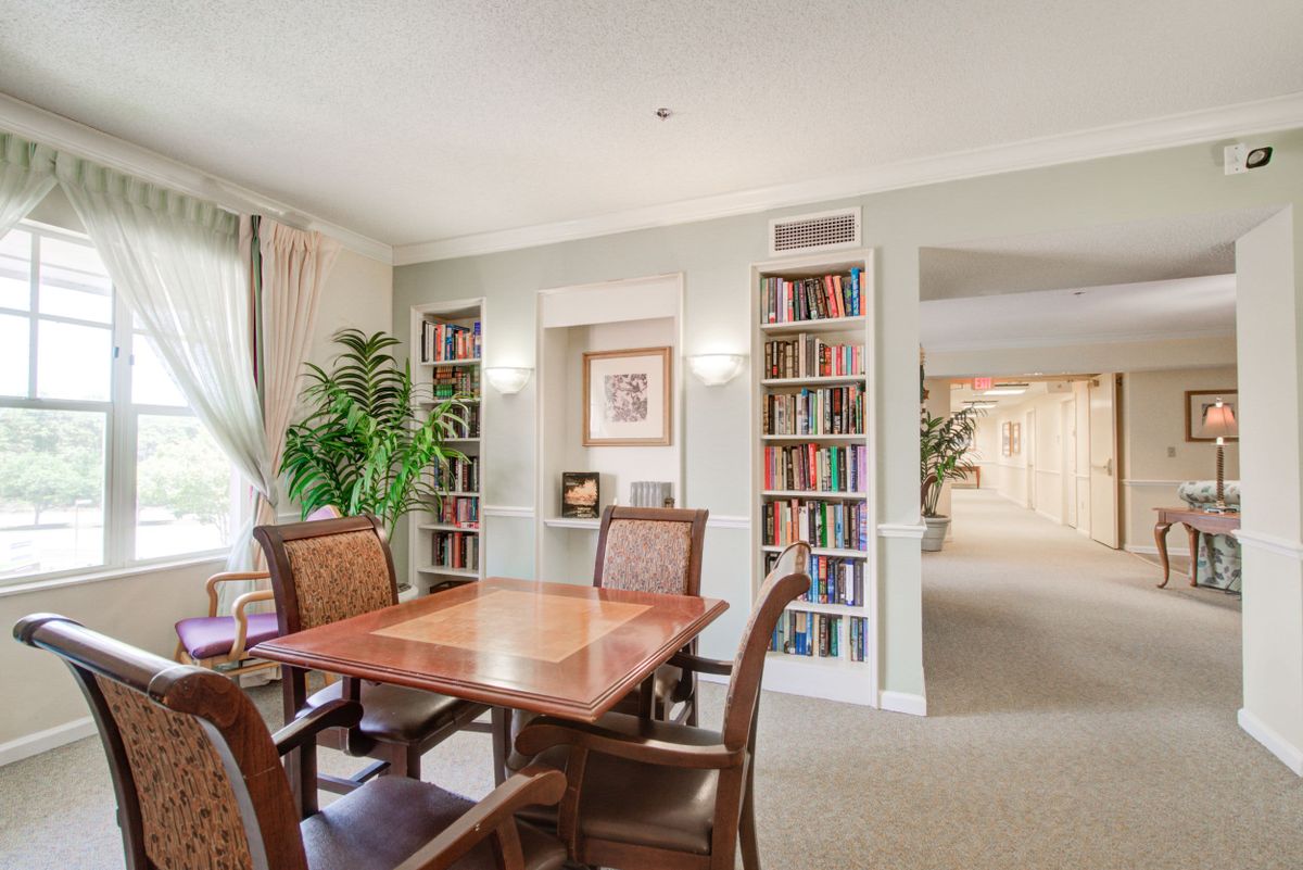 A cozy library room with bookshelves, a table, chairs, and indoor plants.