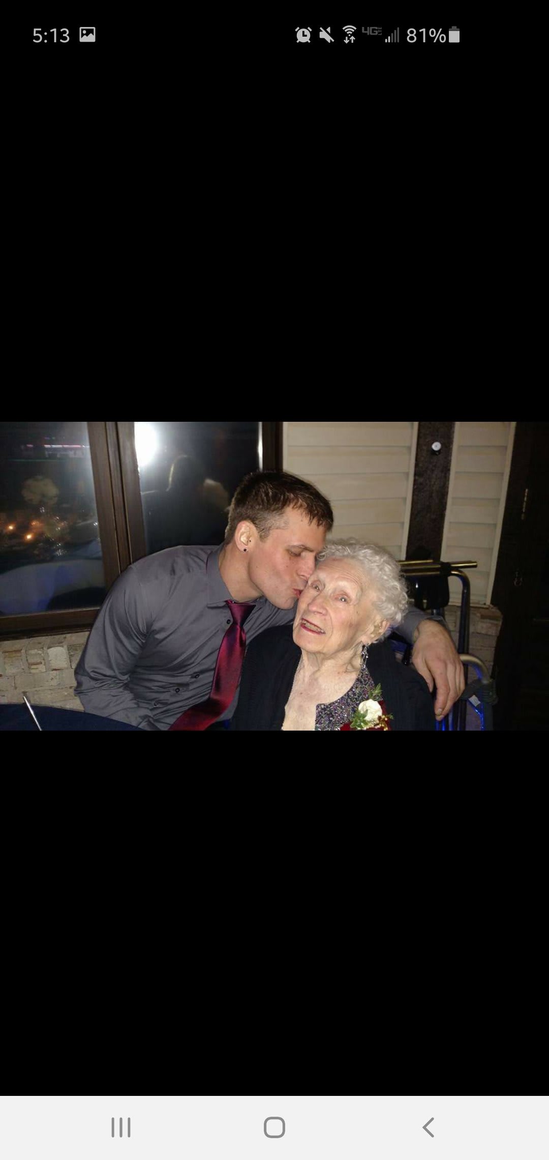 A young man affectionately kisses an elderly woman on the forehead indoors.