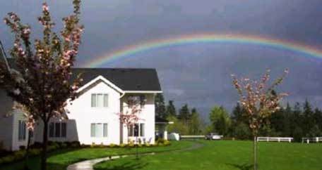 A beautiful rainbow arches over a house in a serene landscape.