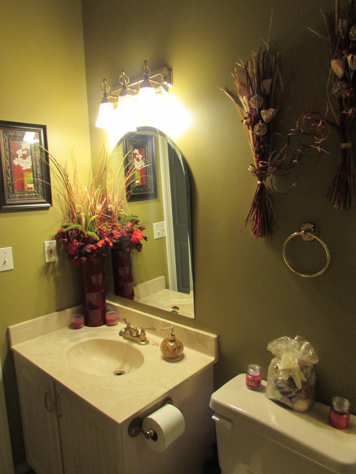 A warmly lit bathroom with decorative flowers, a mirror, and green walls.