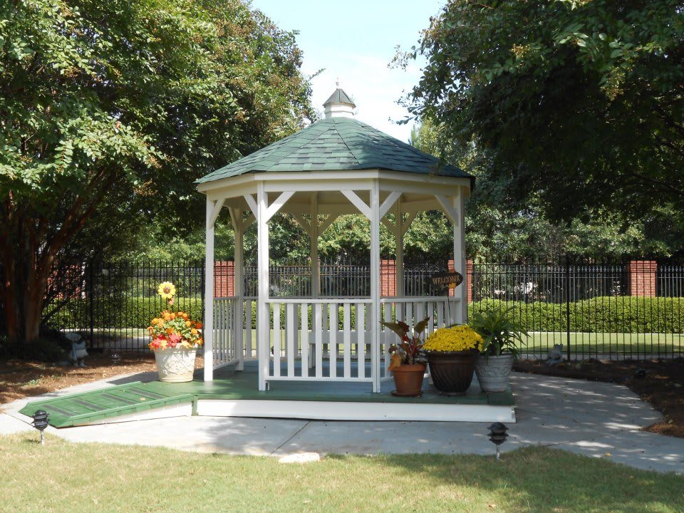 A charming gazebo surrounded by a garden with various potted flowers and trees.