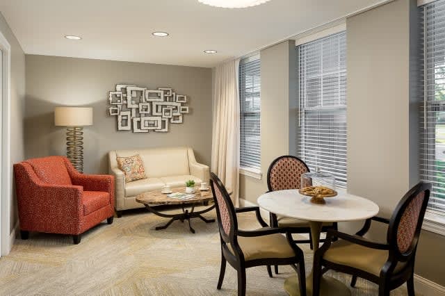 A cozy living room with a sofa, armchair, and dining area, featuring elegant decor and wall art.
