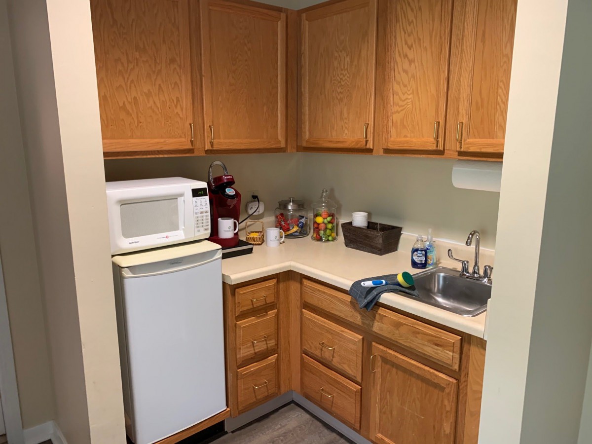 A small kitchen area with wooden cabinets, a microwave, and a mini refrigerator.