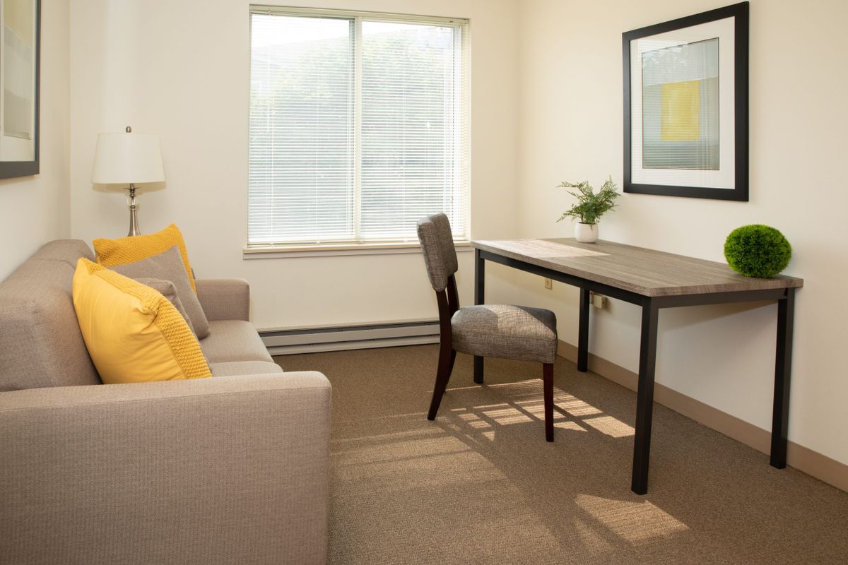 A minimalist office space with a desk, chair, sofa, and natural light from a large window.