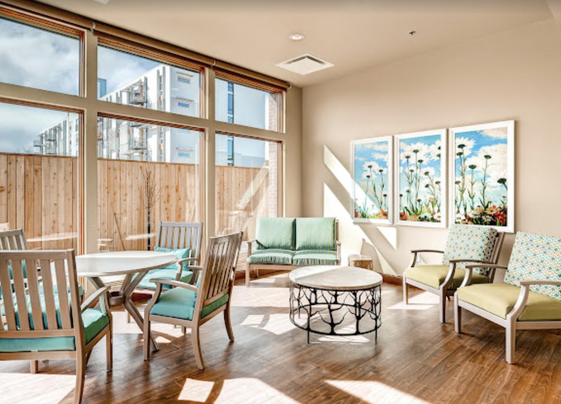 A well-lit modern living room featuring large windows, comfortable seating, and decorative artwork on the walls.