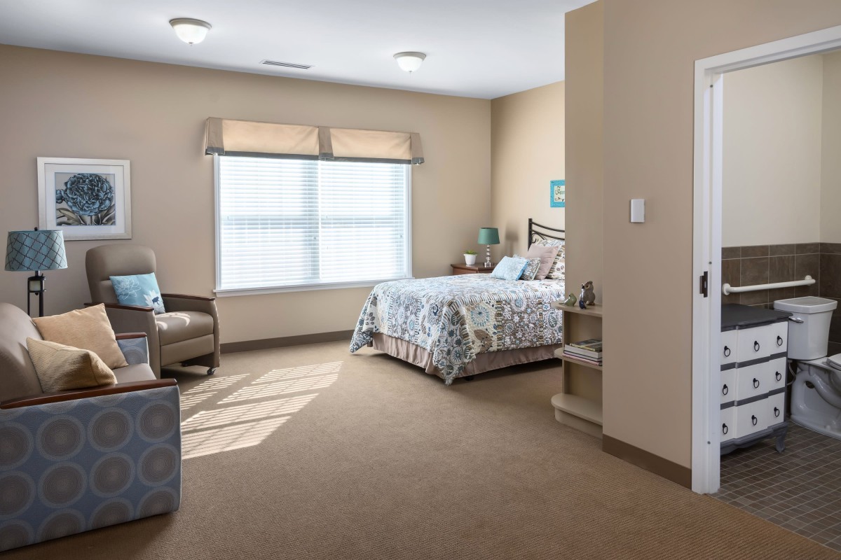 A cozy bedroom with a bed, chair, and window letting in natural light.