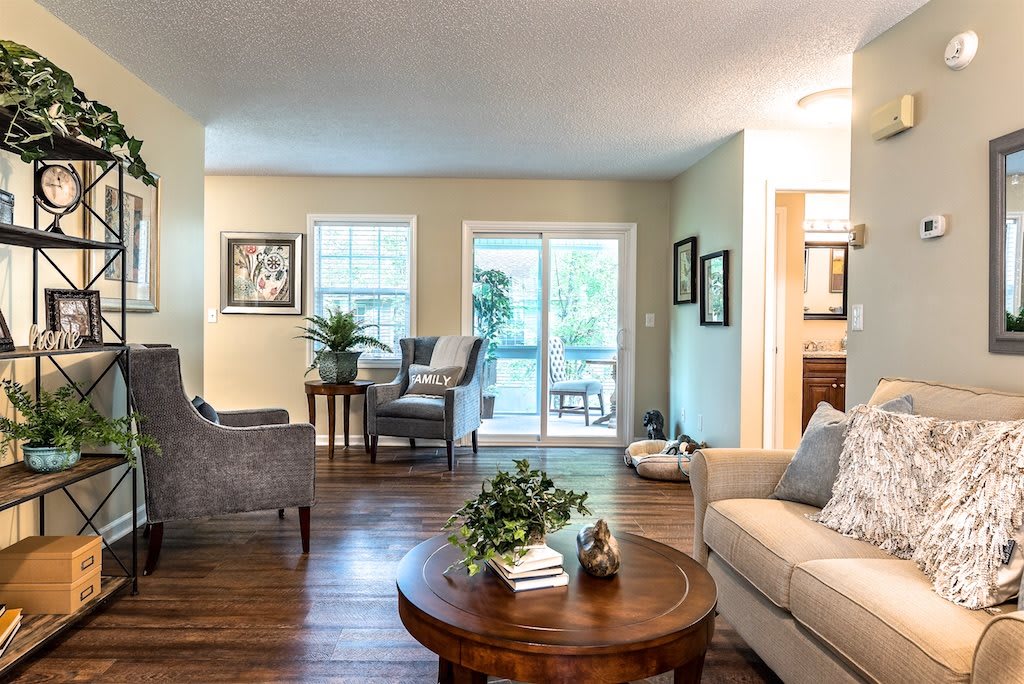 A cozy living room featuring comfortable seating, a coffee table, and natural light from large windows and a sliding door.