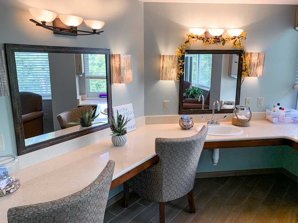 A stylish bathroom vanity setup with two mirrors, comfortable chairs, and elegant lighting.
