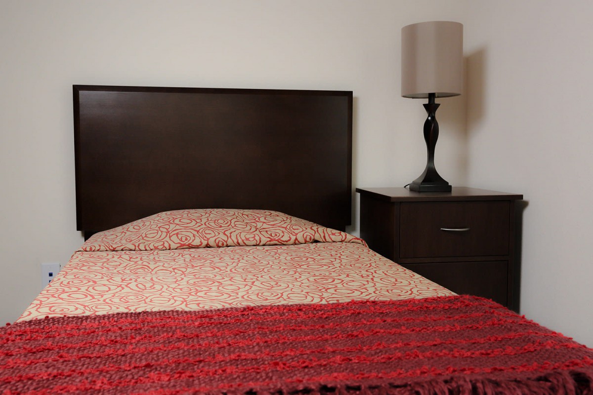 A neatly made bed with a dark wooden headboard and a side lamp on the nightstand.