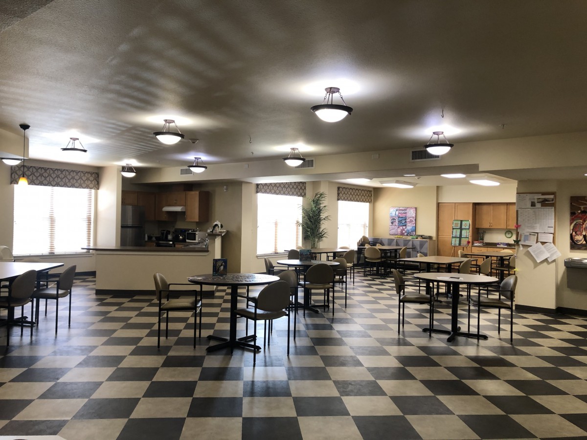 An empty cafeteria with checkered flooring and neatly arranged tables and chairs.