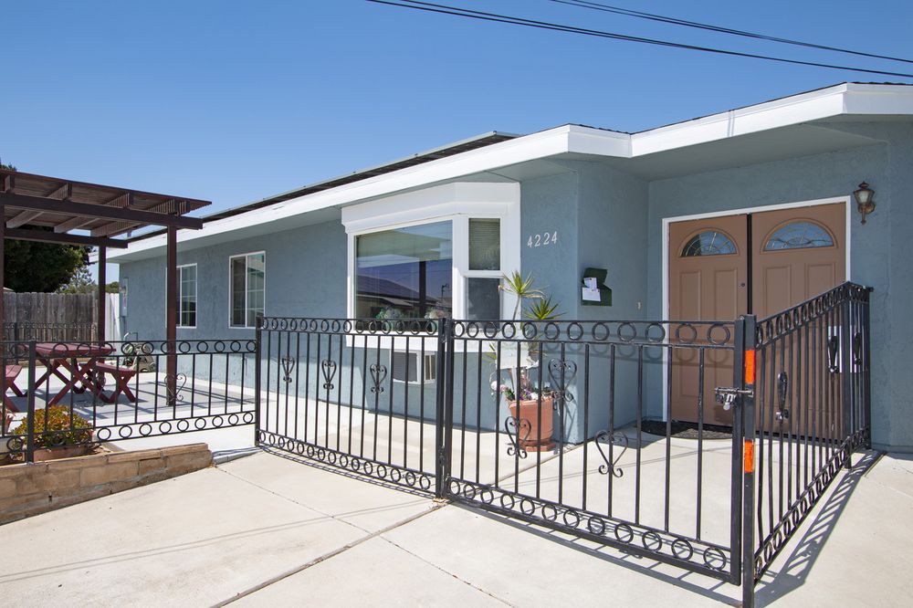 A single-story house with a modern design and a metal fence in front, under a clear blue sky.