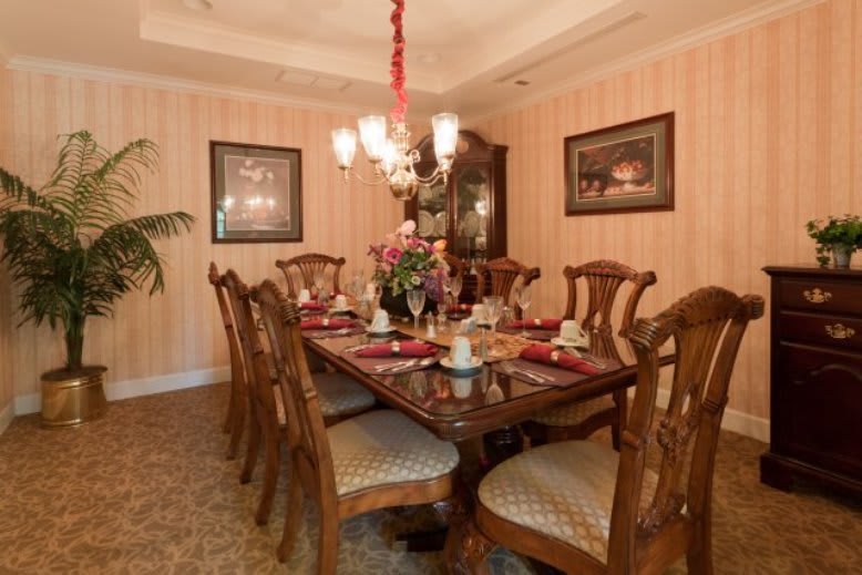 A traditionally styled dining room with an ornate wooden table and matching chairs, elegantly set for a meal under a decorative chandelier.