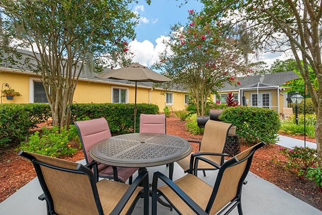 A cozy outdoor patio area with a round table and four chairs surrounded by lush greenery.