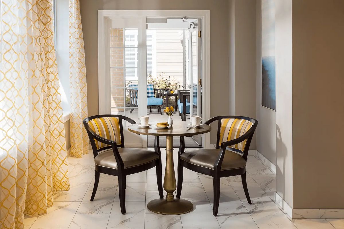 A modern dining area featuring a glass-topped table with two stylish chairs in a well-lit space.