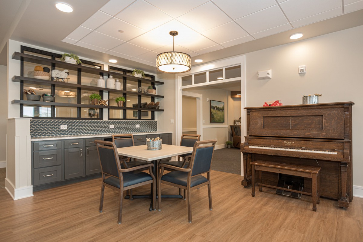 A cozy dining area with a table, chairs, piano, and decorative shelves.