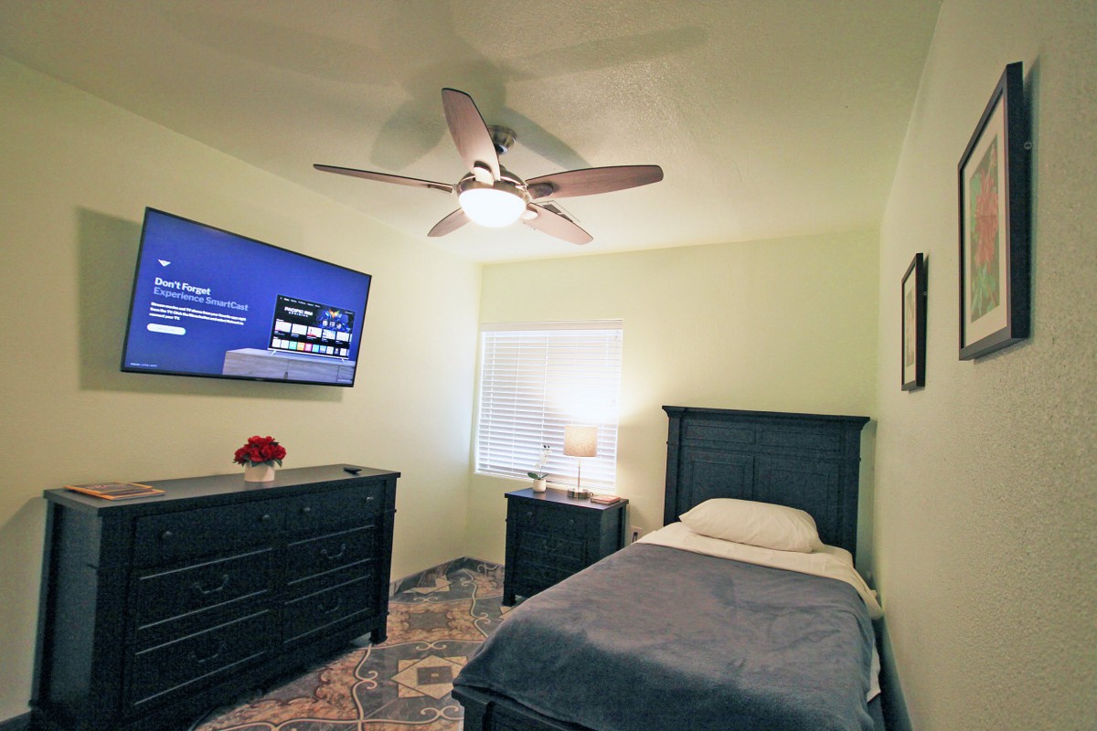 A cozy bedroom featuring a single bed, wall-mounted TV, and dresser.
