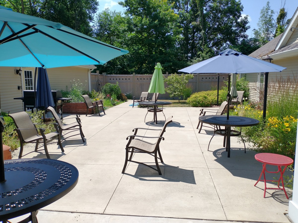 A sunny outdoor patio with tables, chairs, and umbrellas surrounded by greenery.