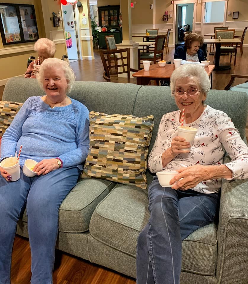 Two elderly women relaxing on a sofa with coffee in a cozy setting.