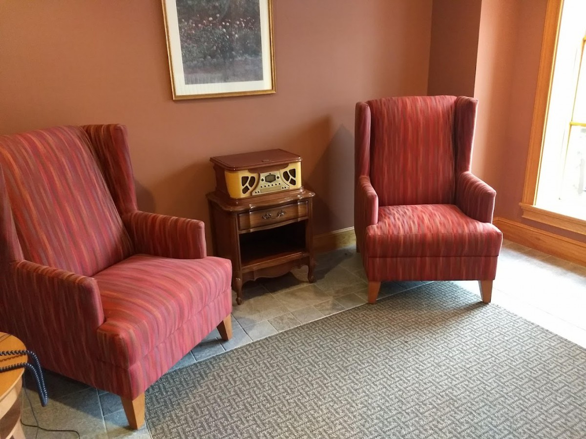 A cozy lounge area with two red striped chairs, a vintage radio on a small wooden table, and a painting hanging on the wall.