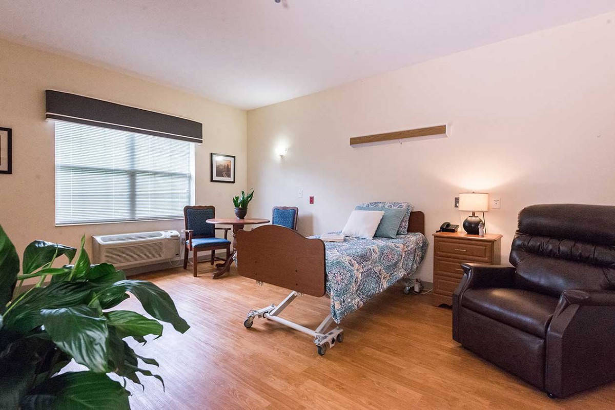 A clean and organized hospital room with a bed, chairs, and a window.